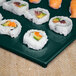 A Tablecraft hunter green rectangular cast aluminum platter with sushi rolls on a table.