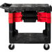 A black Rubbermaid TradeMaster cart with red handles holding a tray and boxes.