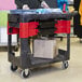 A Rubbermaid black TradeMaster cart with parts bins and boxes on it.