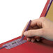 A person holding a pen labeling a red Smead SafeSHIELD legal size folder.