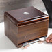 A person's hand opening a wooden box with a brown Vollrath Straw Boss lid inside.