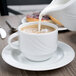 A Schonwald white porcelain cup of coffee with milk being poured into it.