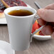 A hand holding a Schonwald white porcelain espresso cup of coffee.
