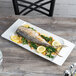 A fish on a Schonwald rectangular white porcelain platter with lemon slices and greens.