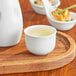An Acopa bright white sake cup filled with liquid on a wooden tray.