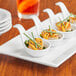 A group of Acopa white porcelain tasting spoons with scallops and green garnish on a table.