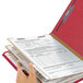 A person holding a red Smead SafeSHIELD legal size classification folder with papers.