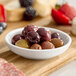 A small white porcelain round sauce cup filled with assorted olives.