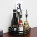 A black wrought iron condiment caddy holding a glass jar of brown liquid, a black bottle, and a glass jar with a metal lid.