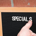 A person pointing to a black Aarco felt message board with the word "specials" written on it.