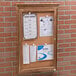 An Aarco natural oak enclosed bulletin board with cork papers attached.