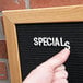 A person pointing at an Aarco black felt message board with oak frame.