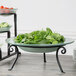 A bowl of greens sits on a Libbey round black metal display frame on a table.