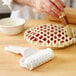 A hand using an Ateco lattice dough cutter to make a pie with a lattice pattern.