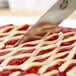 A knife cutting a lattice pie with strawberries.