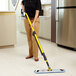 A woman using a Rubbermaid Pulse spray mop to clean a professional kitchen floor.