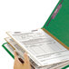 A hand holding a green Smead SafeSHIELD legal size classification folder.