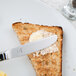 A Libbey Cortland stainless steel bread and butter knife spreading butter on a piece of toast.