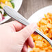 A hand holding a Libbey stainless steel dessert fork over a bowl of pasta.