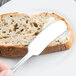 A hand holding a Libbey stainless steel butter knife over a slice of bread.