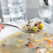 A Libbey stainless steel bouillon spoon holding soup with vegetables.