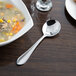 A bowl of soup with a Libbey stainless steel bouillon spoon on a table.