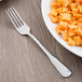 A World Tableware stainless steel utility fork next to a plate of pasta.