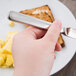 A hand holding a Libbey stainless steel bread and butter knife over a plate of toast and scrambled eggs.
