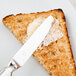 A Libbey stainless steel bread and butter knife spreading butter on a piece of toast.