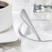 A Libbey stainless steel demitasse spoon in a bowl of sugar next to a cup of coffee.