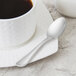 A Libbey stainless steel demitasse spoon on a white plate with a cup of coffee.