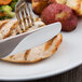 A Libbey stainless steel serrated dinner knife and fork on a piece of chicken.