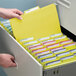 A person holding a yellow Smead file folder in a file cabinet.