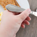 A hand holding a Libbey stainless steel bread and butter knife.