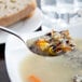 A Libbey stainless steel bouillon spoon filled with soup next to a piece of bread.