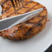 A Libbey stainless steel fluted steak knife and fork on a plate of grilled pork chop.