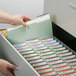 A hand opening a file cabinet drawer to put a Smead file folder inside.