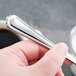 A hand holding a Libbey stainless steel dessert spoon.