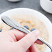 A hand holding a Libbey stainless steel dessert spoon over a bowl of oatmeal.