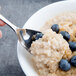A Libbey stainless steel dessert spoon in a bowl of oatmeal with blueberries.