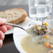 A person's hand holding a Libbey stainless steel bouillon spoon filled with soup over a bowl of food.