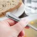 A hand holding a Libbey stainless steel bouillon spoon over a bowl of soup.