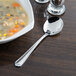 A bowl of soup next to a Libbey Cortland stainless steel bouillon spoon.