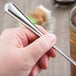 A hand holding a Libbey stainless steel iced tea spoon over a glass of iced tea.