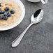 A Libbey stainless steel teaspoon next to a bowl of oatmeal with blueberries.
