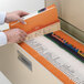 A person opening a file drawer with an orange Smead file folder.
