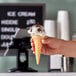 A hand holding a JOY pointed bottom cake cone filled with ice cream.