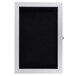An Aarco black message board with a white frame and hinged door.