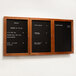 A black wooden bulletin board with a cherry wood frame and three black menu boards with white text.