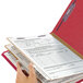 A hand holding a Smead red classification folder with documents.